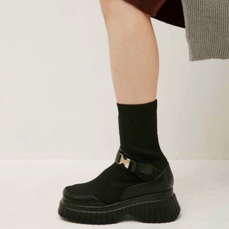 トレンド感と機能性が合わさったミドル丈のニットスニーカーブーツ。  ニット×レザーで高級感を醸し出しながら、ニットならではの伸縮性でストレスフリーな履き心地を実現。脚にしっかりとフィットする素材なので、足元を細くすっきり見せるシルエットも特徴的です。  スポーティーさを感じさせるバックル使いで、緩さ加減を自分好みに調節できるのも嬉しいポイント。さらに、軽量なトラックソールを使っているため、安定感や美脚効果をもたらしてくれます。  ニュートラルなブラックカラーのみでの展開になります。